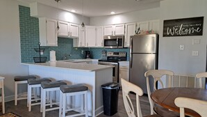 A modern kitchen with white cabinets, a central island with bar stools, a stainless steel refrigerator, and a microwave.