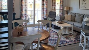 A living room with a dining area, a ceiling fan, patterned curtains, a sofa, a coffee table, and a rug.