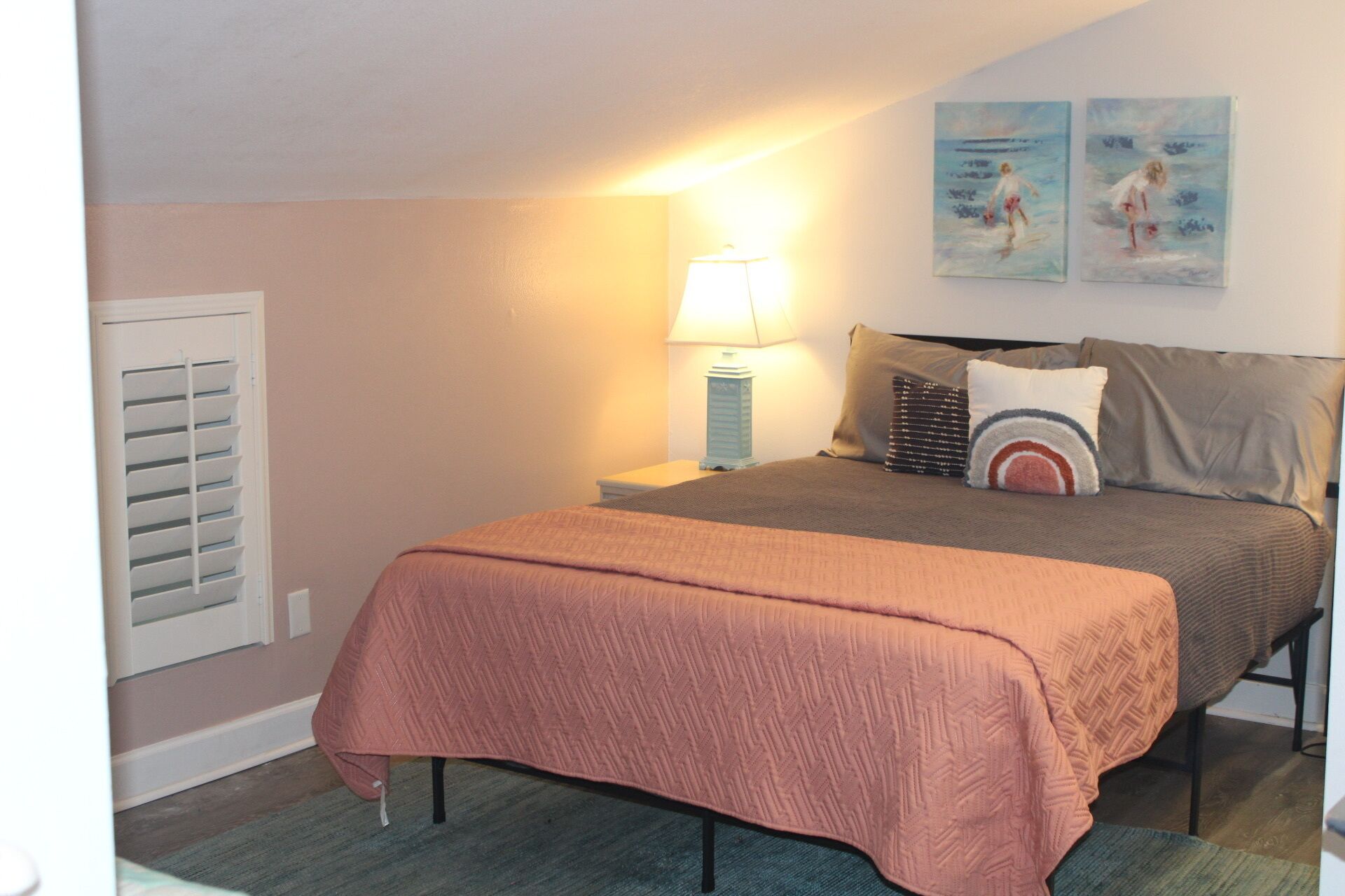 A bedroom with a bed, a nightstand, a lamp, and two wall art pieces.