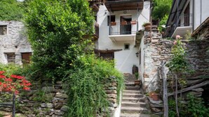 Un bâtiment traditionnel en pierre, doté d’un balcon, entouré d’une végétation luxuriante et agrémenté d’un escalier en pierre.