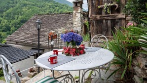 Une table ronde en métal recouverte d’une nappe blanche, deux tasses rouges en forme de cœur et un vase avec des fleurs violettes.