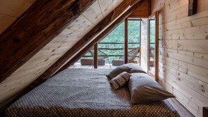 Une chambre confortable située sous les toits, avec un plafond en pente, des poutres apparentes et une grande fenêtre donnant sur le paysage extérieur.