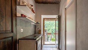 Un couloir étroit, avec un coin cuisine sur la gauche, comprenant un meuble en bois et un plan de travail. Un tapis à motifs recouvre le sol et mène à une porte vitrée qui donne sur un balcon offrant une vue sur la verdure.