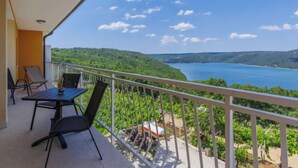 Un balcon avec une table et des chaises, offrant une vue panoramique sur un lac et des collines.