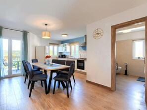 A modern kitchen with a dining area, wooden flooring, and a view through a glass door.