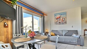 Een moderne woonkamer met een eethoek, een grijze bank en een schilderij van een fiets.