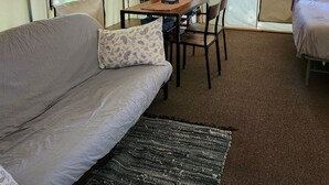 Una habitación con carpa, un sofá, una mesa con sillas, una cafetera y una cama.