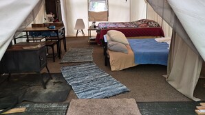 Alojamiento en tienda de campaña con cama, escritorio, silla, lámpara y una mesita.