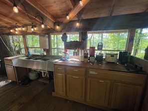 A rustic kitchen with wooden cabinets, a stainless steel sink, and a window overlooking greenery. - Cozy Homestead Living in a Treetent getaway (Grandview)