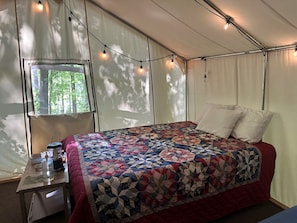 Ein Zeltraum mit einem Bett, einem Tisch und einer Wasserflasche, sowie Lichterketten.
