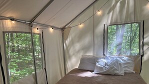 Une tente équipée d’un lit, de guirlandes lumineuses et d’une fenêtre donnant sur la forêt.