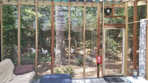Una habitación con un ventanal grande con vistas a un bosque, una cama, un extintor y un ventilador.