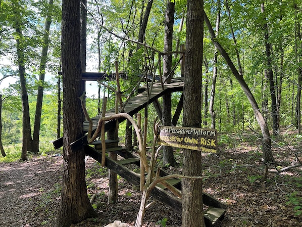 Une plateforme en bois, surmontĂ©e dâun panneau dâavertissement indiquant un danger, et entourĂ©e dâarbres.