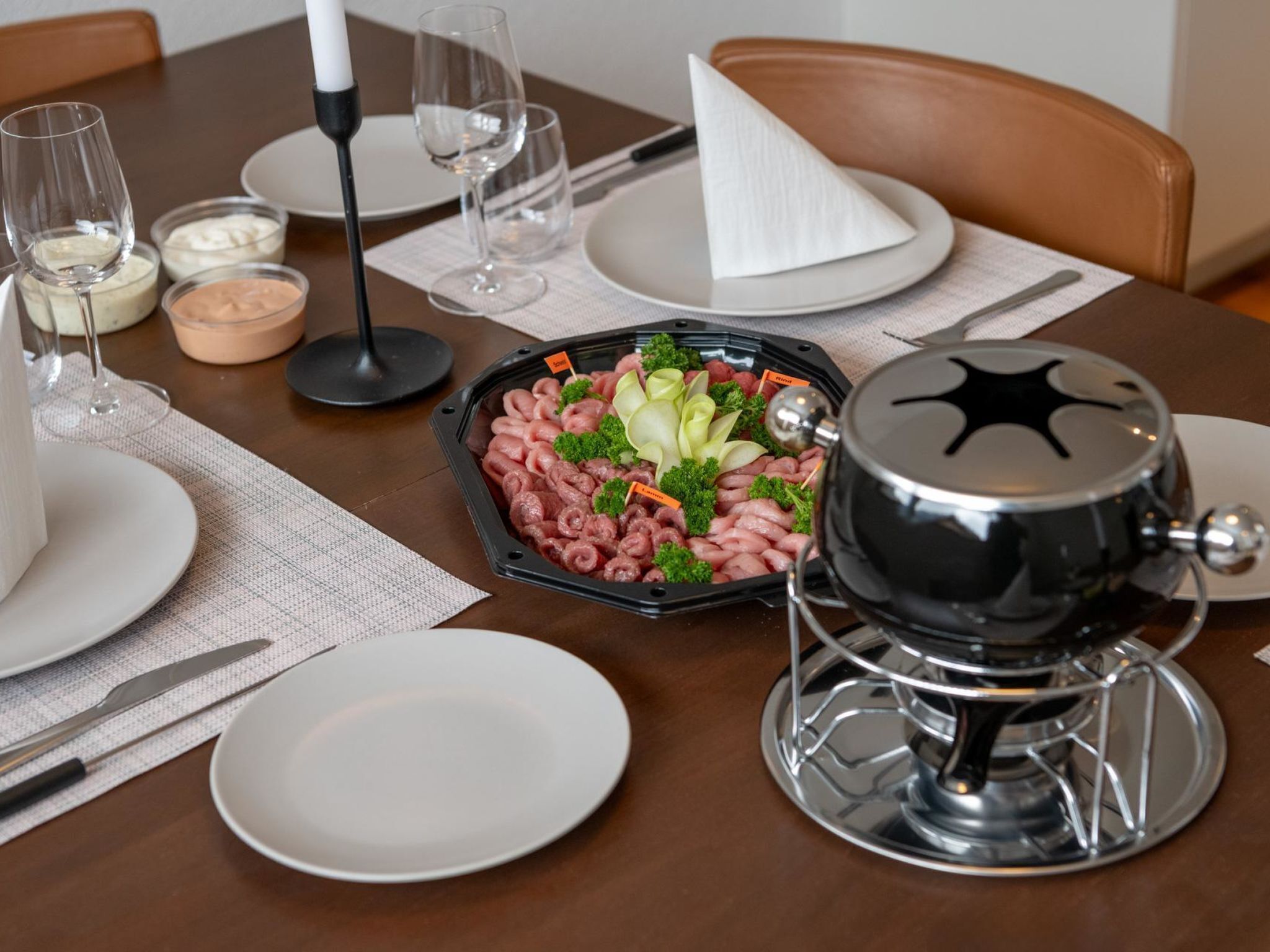 Una mesa de comedor lista para una comida, con una tabla de embutidos, copas de vino y una tetera.