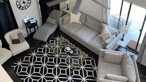 Un salon moderne doté d’un ventilateur de plafond, d’un tapis à motifs géométriques et d’un canapé agrémenté de plusieurs coussins.