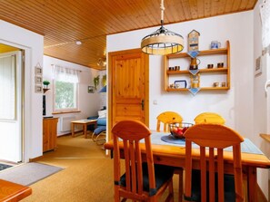 A cozy room with a wooden ceiling, a dining table with chairs, a hanging light fixture, and a shelf with various items. - Vacation home Czaja by Interhome (Zinnowitz)