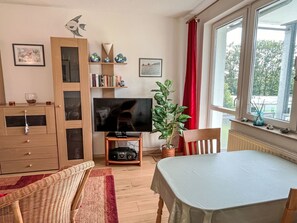 A living room with a television, bookshelf, red curtains, and a window with a view of trees. - Karsten by Interhome (Zinnowitz)