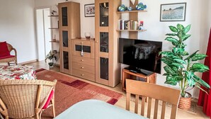 A living room with a TV, wooden furniture, a bookshelf, and a potted plant. - Karsten by Interhome (Zinnowitz)