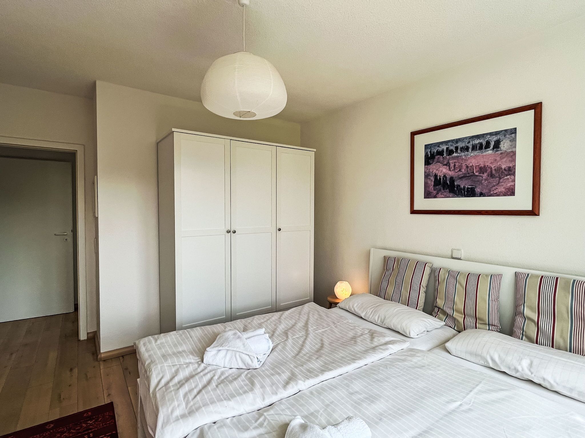 A bedroom with a bed, a wardrobe, a painting, and a bedside lamp.