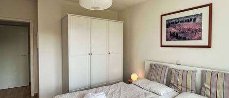 A bedroom with a bed, a wardrobe, a painting, and a bedside lamp.
