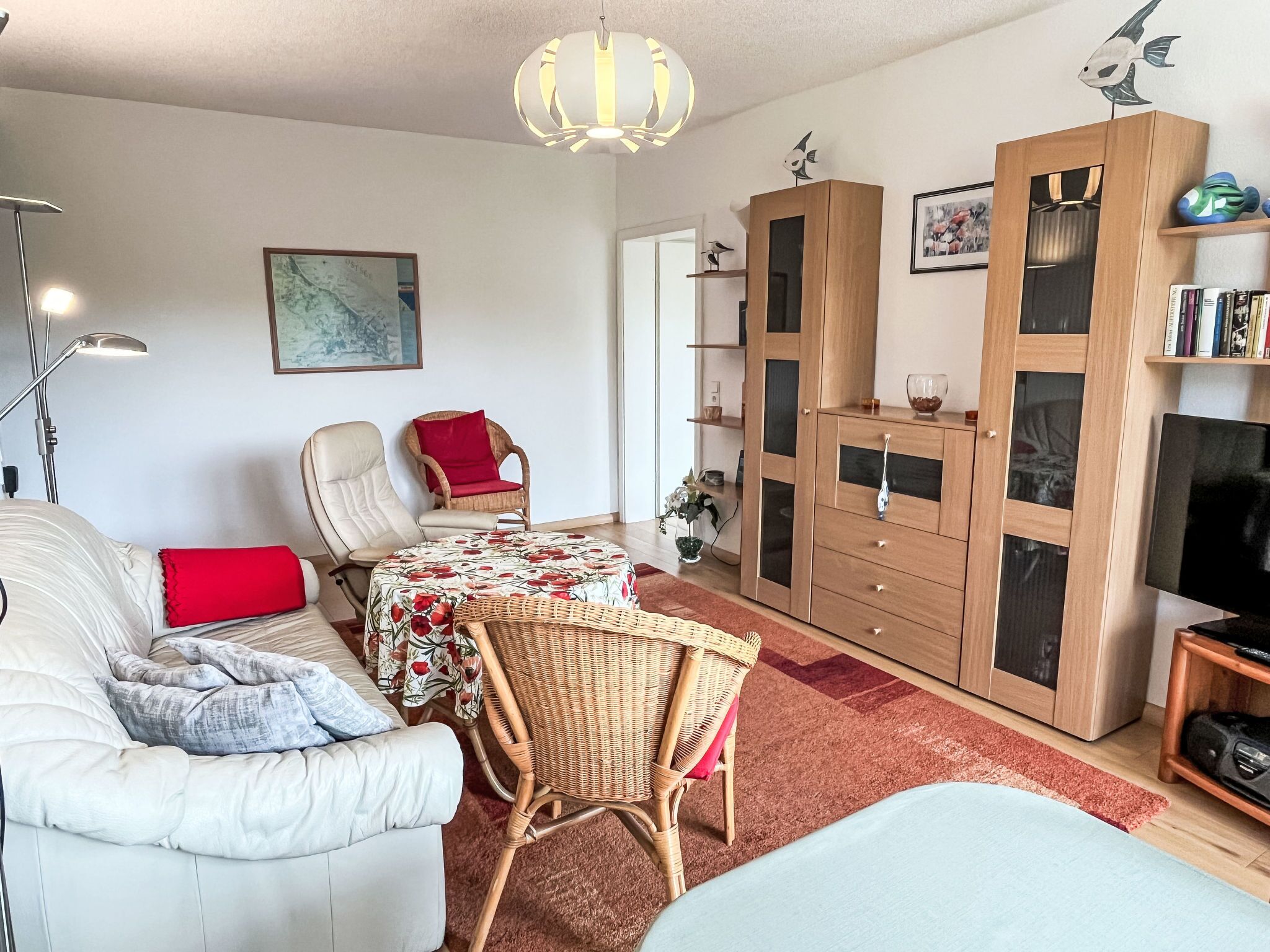 Un salon comprenant un canapé, un fauteuil, une table recouverte d’une nappe à motifs floraux, une bibliothèque et un téléviseur.