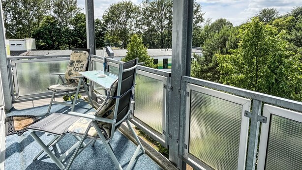 A balcony with a table and chairs, a chair with a bag, and a metal railing. - Karsten by Interhome (Zinnowitz)