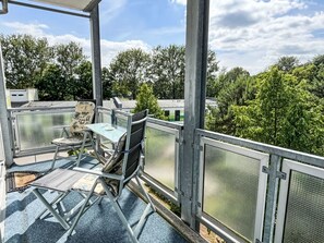 En balkon med et bord og stole, en stol med en taske, og gelænder af metal.