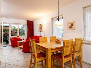 A dining area with a wooden table and chairs, a red sofa, and a window with curtains. - Vacation home Conny by Interhome (Koserow)