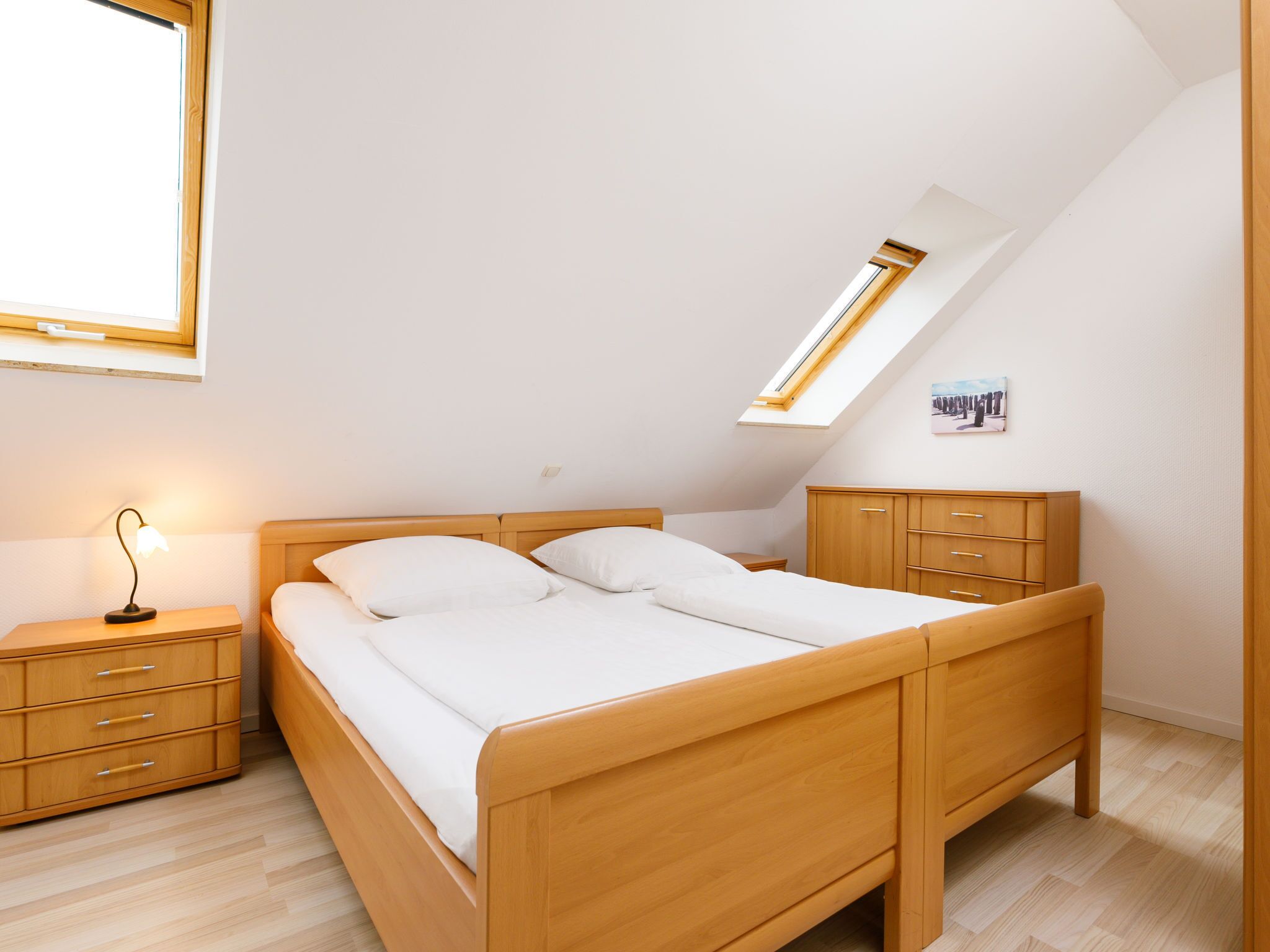 Ein Schlafzimmer mit einem hölzernen Bett, einem Nachttisch, einer Kommode und einem Dachfenster.