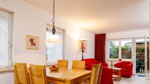 A dining area with a wooden table and chairs, a red sofa, and a red armchair. There are two windows with curtains, and a lamp hangs from the ceiling. - Vacation home Susi by Interhome (Koserow)