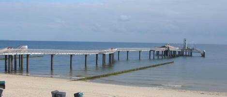 A beach with a pier extending into the sea, featuring several beach chairs and umbrellas.