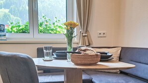 A dining area with a table, chairs, a bowl of bread, a vase with flowers, and a view of greenery through a window. - Apartement Haus Dankl by Interhome (Fusch)