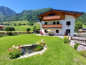 Ein zweistöckiges Gebäude mit Balkon, einem kleinen Teich und einer Bergkulisse.
