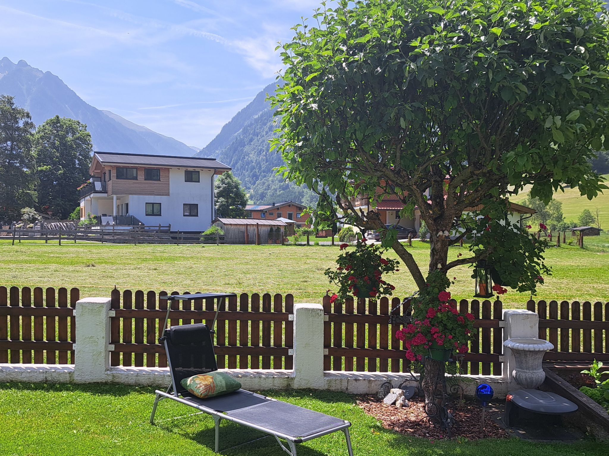 A grassy area with a wooden fence, a lounge chair, and a tree with flowers.