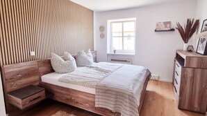A modern bedroom with a wooden headboard, a bed with patterned bedding, a nightstand, a fluffy rug, a wooden dresser, and a window with natural light. - Fantastic time-out vacations for families - fun and relaxation for young and old! (Bad Lauchstädt)
