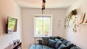 A modern living room with a sectional sofa, a wooden coffee table, a TV mounted on the wall, a window with a view of greenery, and a hanging plant. - Fantastic time-out vacations for families - fun and relaxation for young and old! (Bad Lauchstädt)