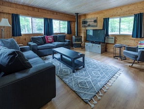 A cozy cabin interior with a sofa, a coffee table, a television, and a fireplace.