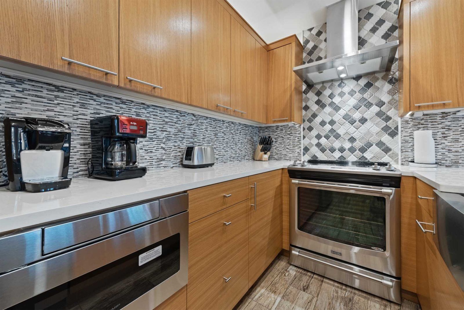 A modern kitchen with wooden cabinets, a stainless steel oven, a coffee maker, and a toaster.