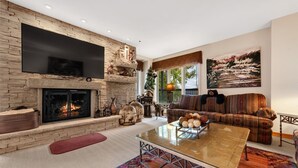 A modern living room with a stone fireplace, a flat-screen TV, a sofa, and a coffee table. - Beaver Creek Centennial 2 Bedroom #17 (Avon)