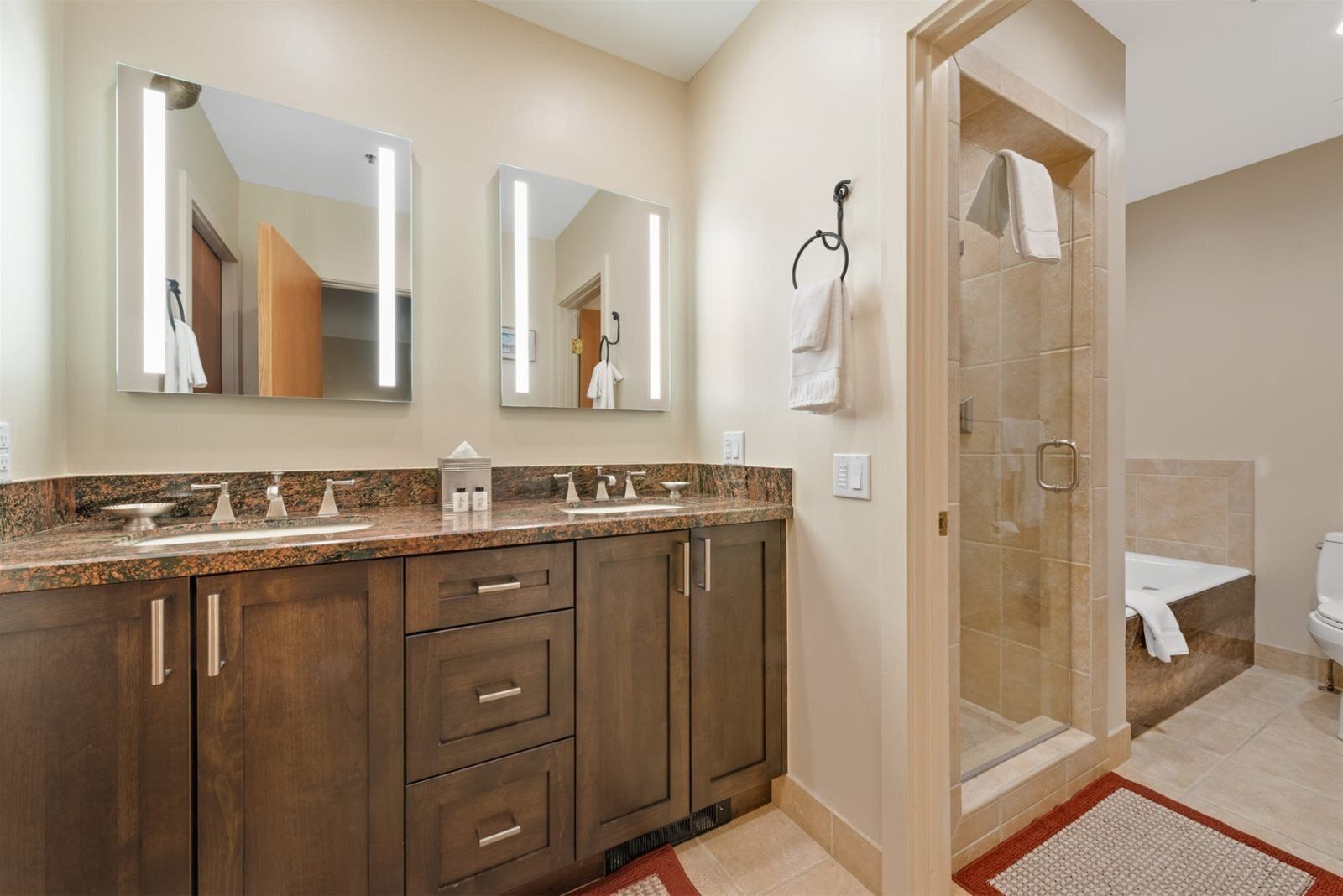 A modern bathroom with a double sink vanity, large mirrors, a glass shower enclosure, and a toilet.