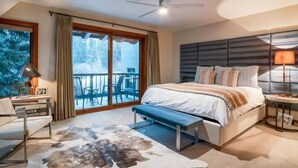 A bedroom with a bed, a bench, a desk, a lamp, and a view of the outdoors. - Beaver Creek Village Ski In, Ski Out 3 Bedroom (Avon)