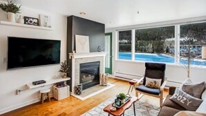 A modern living room with a fireplace, a large TV, and a view of a swimming pool. - Lakeside Village 1 Bedroom Condo in Lakeshore Complex (Keystone)