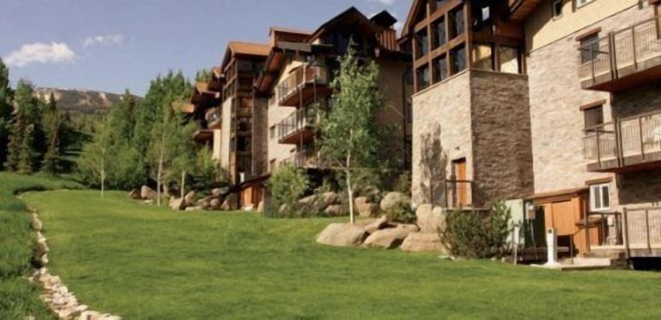 A row of multi-story buildings with balconies, surrounded by a well-maintained grassy area and trees.