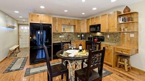 A compact kitchen with wooden cabinets, a black refrigerator, a microwave, and a dining table set with wine glasses and fruit. - Snowmass Village 1 Bedroom Premier Condo at Crestwood (Snowmass Village)