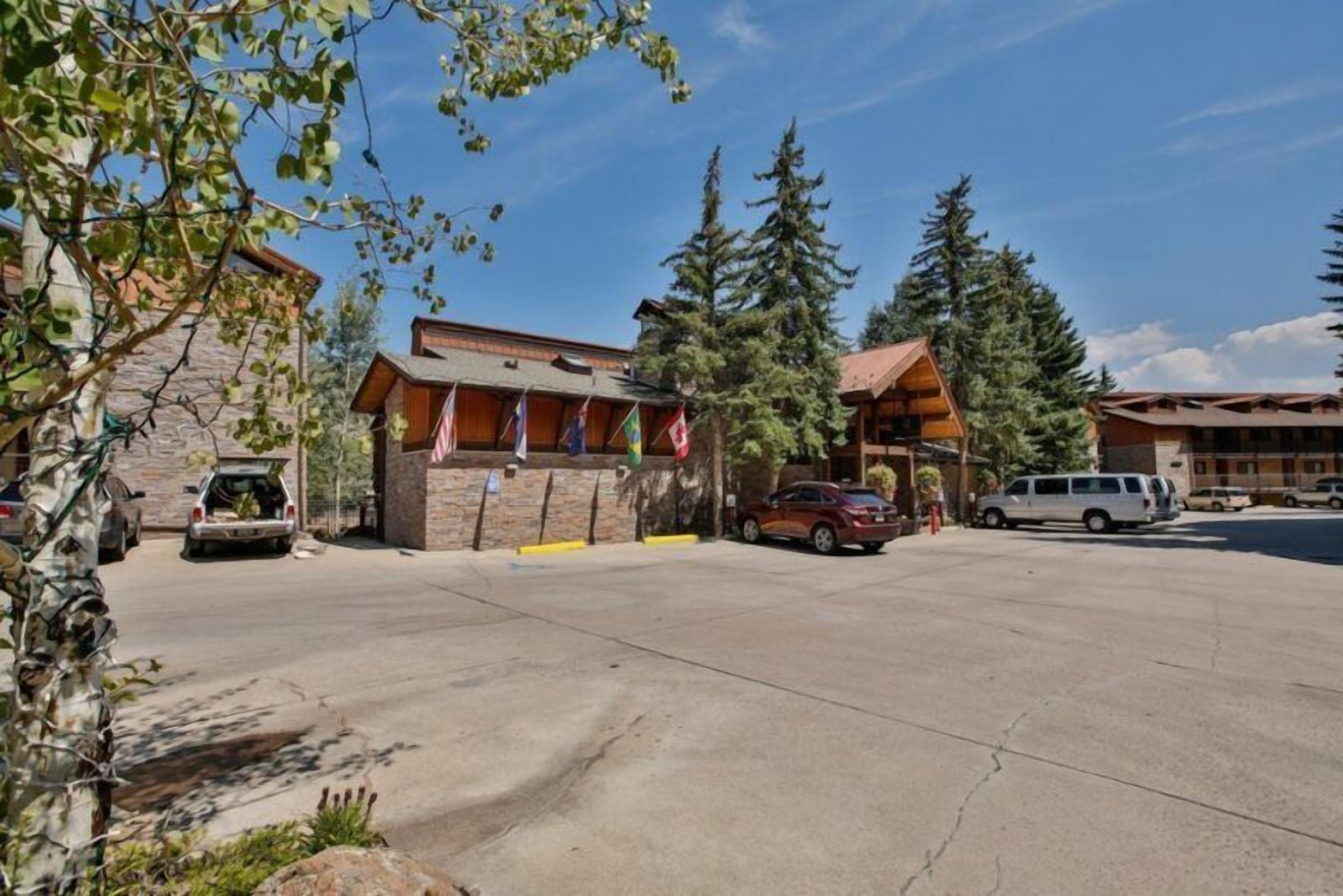 A lodge with a stone facade, wooden exterior, and a parking area with cars.