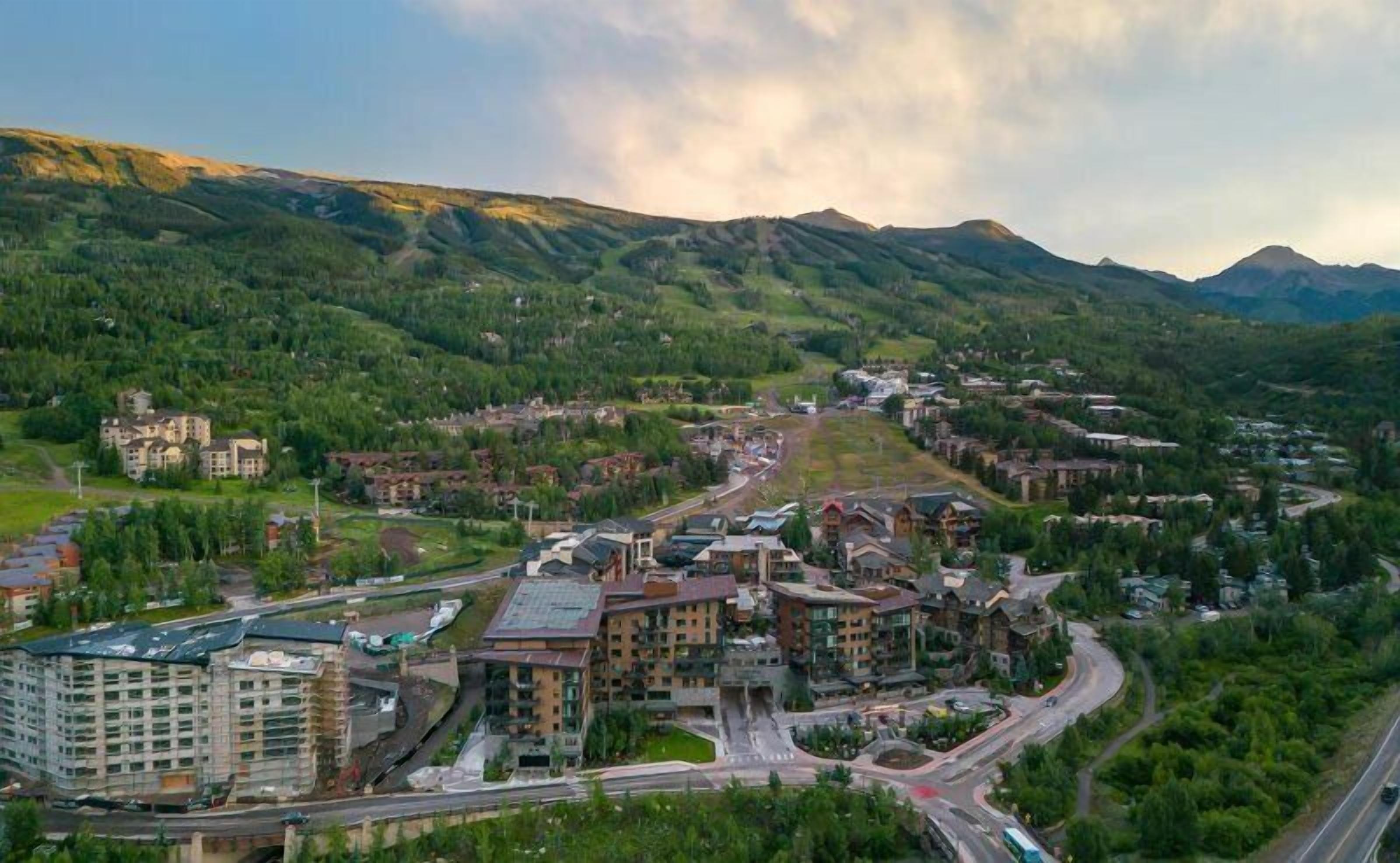A mountainous town with a mix of residential and commercial buildings, roads, and green hills.