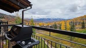 A balcony with a grill, overlooking a mountainous landscape with autumn foliage.