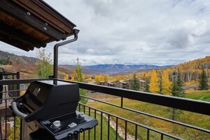 Un balcón con una parrilla, con vistas a un paisaje montañoso con follaje otoñal.