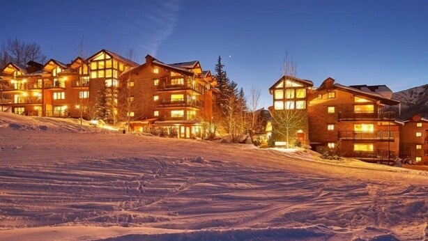 A multi-story lodge with large windows and a ski slope in the foreground.