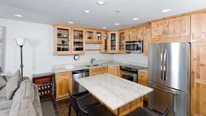 A compact kitchen with wooden cabinets, stainless steel appliances, and a marble countertop. - Snowmass Village 3 Bedroom Premier Condo - Crestwood (Snowmass Village)